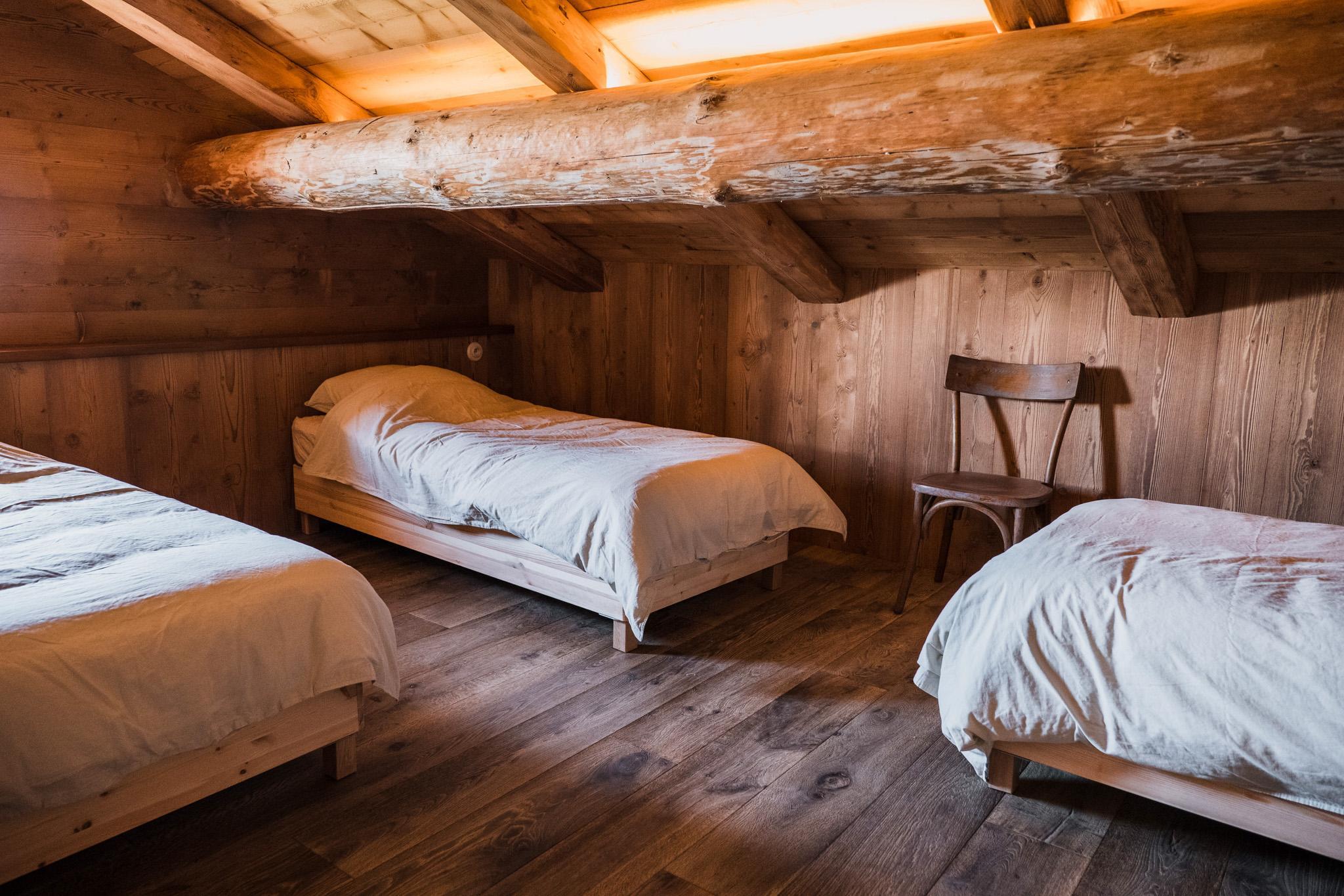 Chambre sous les combles de la ferme d'alpage Grand Montagne, lits individuels et poutraison d'origine